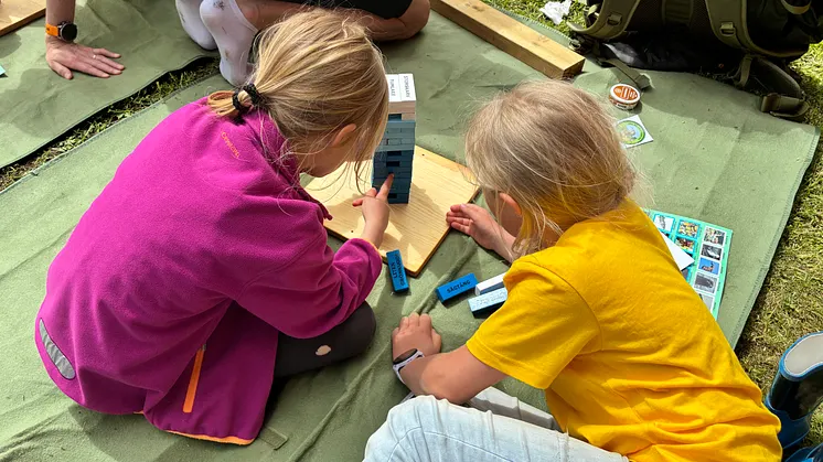 Två barn sitter på en filt och spelar ett jengaspel.