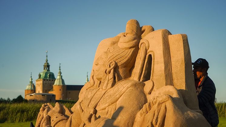 En konstnär arbetar med en stor sandskulptur.