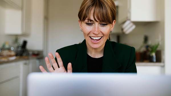 Kvinna som sitter framför en dator och vinkar till deltagarna på det digitala mötet