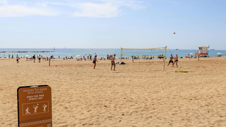 Foto på personer som spelar beachvolleyboll och andra som solar på en sandstrand och badar i havet.