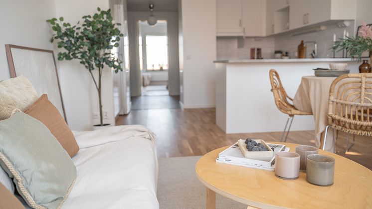Nybyggd inredd lägenhet med öppen planlösning. Soffa och soffbord i förgrunden. Kök och matplats i bakgrunden. 