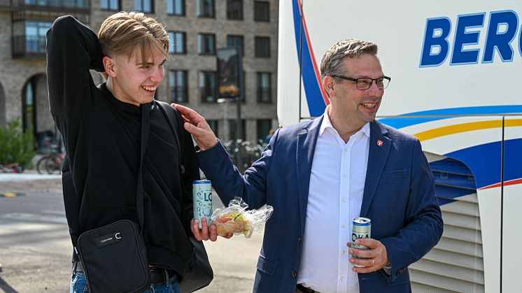 En man och en ung kille i tonåren står bredvid en buss och skrattar tillsammans.