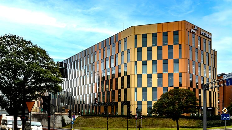 En modern kontorsbyggnad med fasad i rutmönstrade glas- och metallpaneler i nyanser av orange, guld och svart. Byggnaden har 