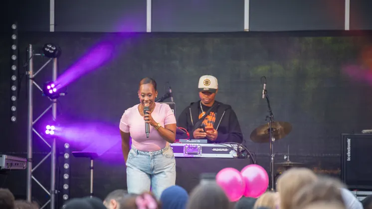 En kvinna på scenen som sjunger inför publik. I bakgrunden står hennes DJ.
