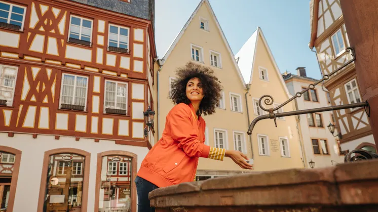 En ung kvinde står ved et springvand i Mainz’ gamle bydel. I baggrunden ses traditionelle bindingsværkshuse.