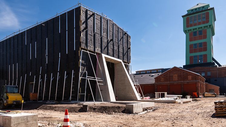 zu sehen ist eine Werkhalle, die gerade im Entstehen ist, dahinter ein Förderturm des Bergbaumuseums in Oelsnitz