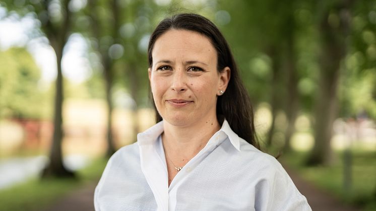 Kvinna i vit blus i en allé med gröna träd