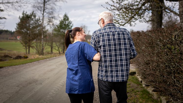 Äldre man går på skogsväg med stöd av hemtjänstpersonal