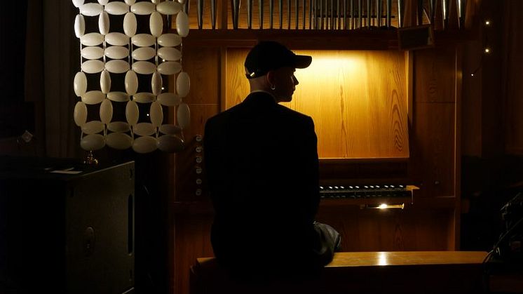 Musikkonstnären Arvid Kraft sitter framför en orgel i dunkel belysning. Foto: Lydia Liljegren.