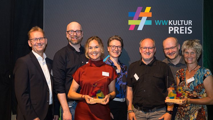 Die Jury-Mitglieder Jürgen Noch (l.) und Dr. In Jana Duda (4.v.l.) gratulieren Kulturamtsleiter Maximilian Zindel,  Julia Ures, Thorsten Hennig, Olaf Menne (alle 0525.1fallsreich) und Sabine Kramm (stellvertretende Bürgermeisterin Stadt Paderborn)​