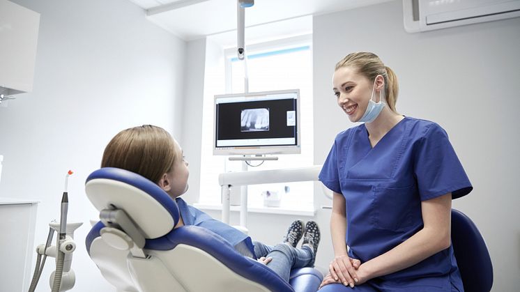 Leende tandvårdspersonal med ung patient på klinik.