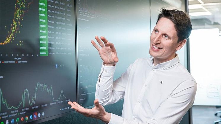 A man is standing in front of a board with charts and numbers explaining something