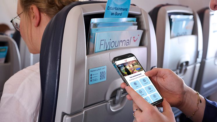 Händer som håller i en iPhone och scrollar i TUIs underhållningssystem i telefonen. I en flygkabin.