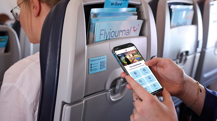 Matkustaja käyttää älypuhelinta lennolla; istuintaskussa Flyjournal-lehti ja digitaalinen  viihdetarjonta 