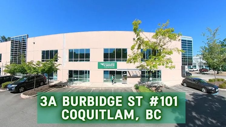 A wide angle view of a reddish beige building with many windows. There is a "Camfil - sign with white text, green background