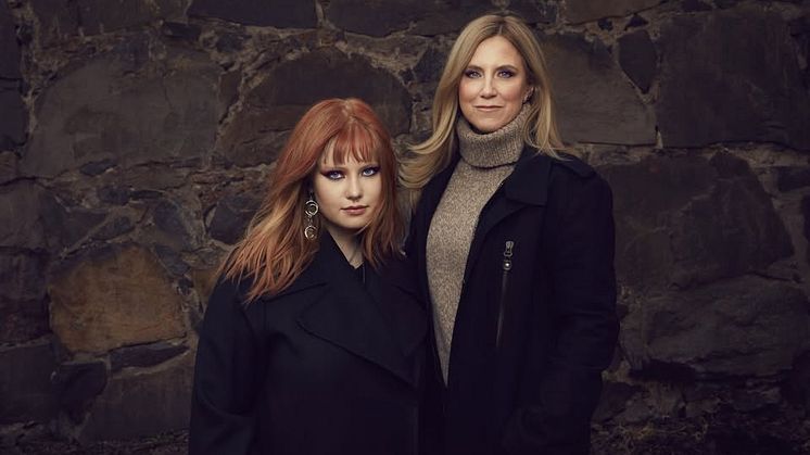 Bild på Tilda och Frida i mörka kläder och mörk bakgrund. Tilda har mycket smink och rött hår. Båda tittar in i kameran.