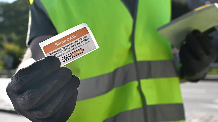 Person i reflexväst som håller fram dekal som talar om att bilen har slitna däck.