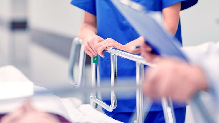 Vårdpersonal hjälper patient som ligger på en brits.