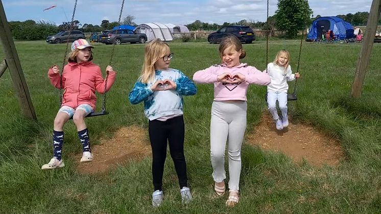 Two girls making hearts with their hands, and two more girls on swings behind them