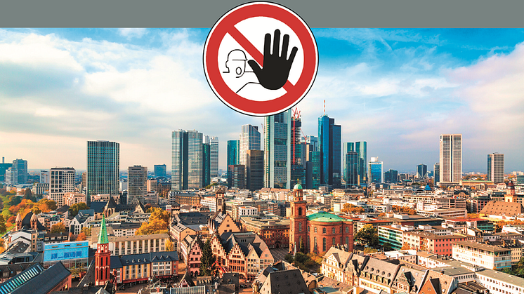 Luftaufnahme einer Stadt mit modernen Hochhäusern und historischen Gebäuden, darüber ein Sicherheitszeichen als Warnhinweis –