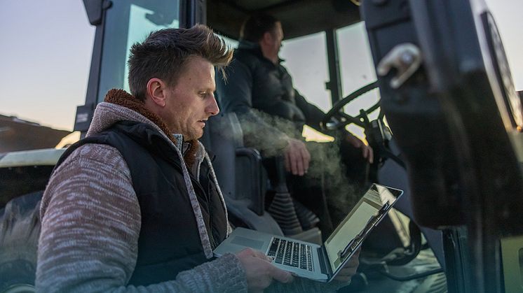 Män med lapptopp och traktor i gryningsljus