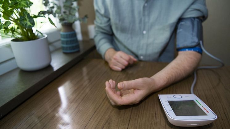 Man mäter sitt blodtryck med en digital blodtrycksmätare vid ett bord