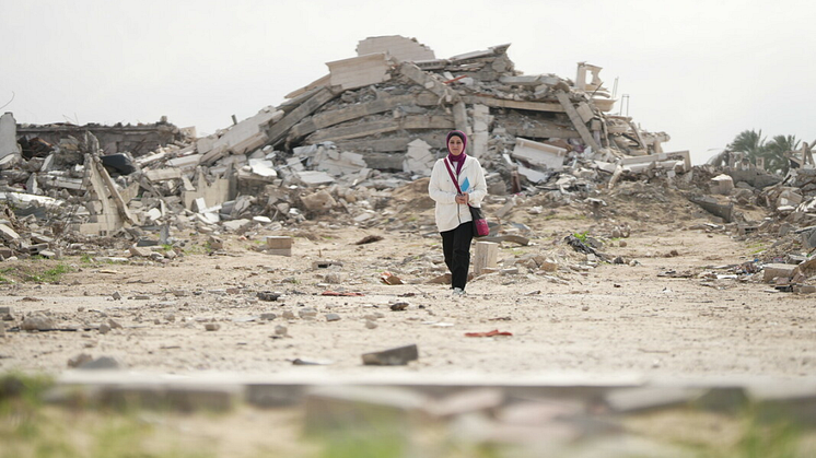 Fidaa Shurrab,  går framför en förstörd byggnad i Gaza på väg till jobbet som projektledare.  Foto: Alef Multimedia