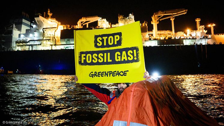 Ein Greenpeace-Aktivist auf einer Schwimminsel mit dem Banner "Stop Fossil Gas" vor dem LNG-Tanker Celsius Gandhinagar im Hafen von Brunsbüttel. Foto: Greenpeace