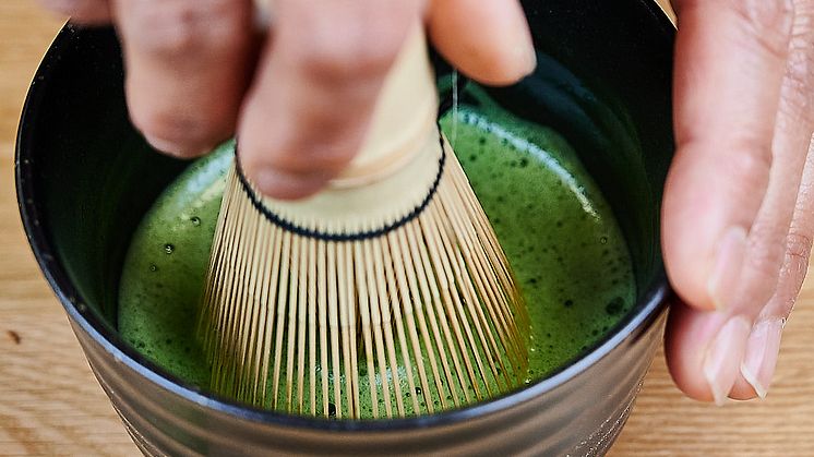 Hand using a matcha whisk to prepare matcha in a black bowl.