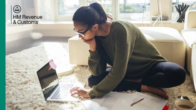 Person sitting on the floor at home using a laptop, with paperwork nearby, accessing online tax services.