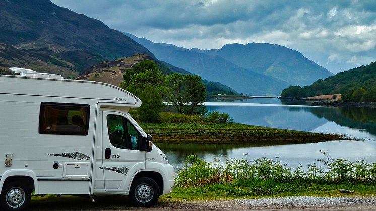 autocamper ved en sø med bjerge i baggrunden.