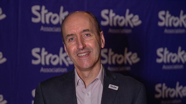 Smiling suited man in front of Stroke Association banner