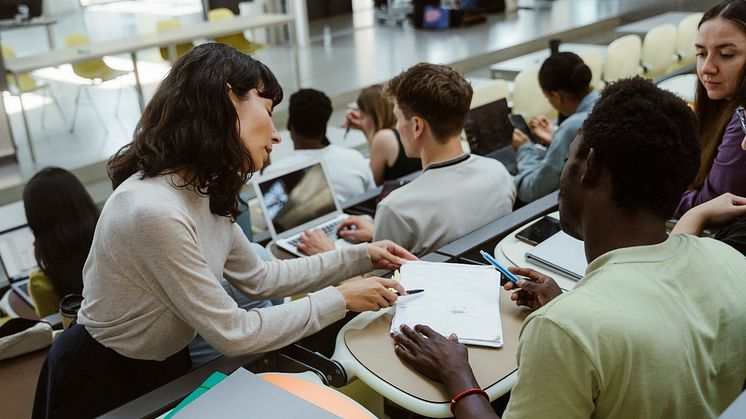 Eine Lehrkraft gibt einem Studenten im Hörsaal HInweise