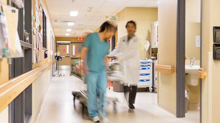 Vårdpersonal drar en säng i sjukhuskorridor