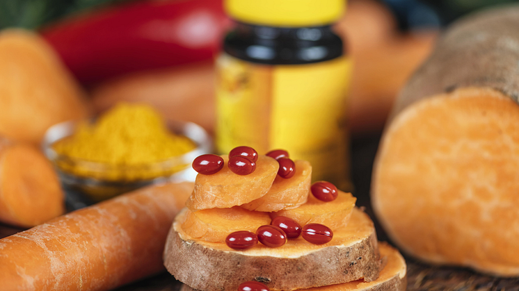 Vitamin B12 supplement capsules on sweet potato slices with carrots, turmeric, and a vitamin bottle.