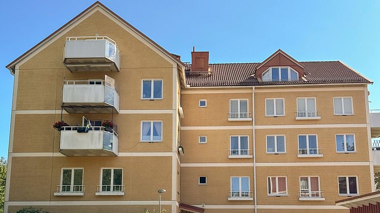 Ett gult flerbostadshus med balkonger på Minervavägen 8E i Häggvik en sommardag.