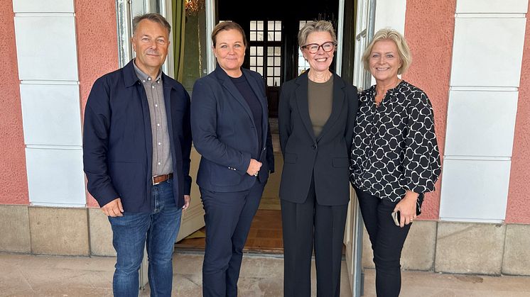 Tre kvinnor och en man står på rad och tittar in i kameran.  