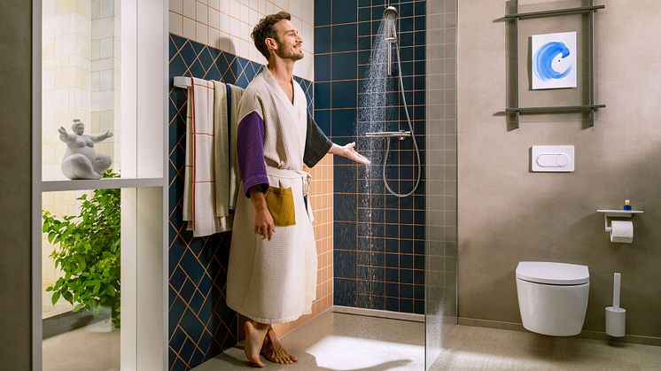 Ein Mann steht mit einem Bademantel in der Dusche und halt seine Hand in den Wasserstrahl einer Handbrause von Hansgrohe