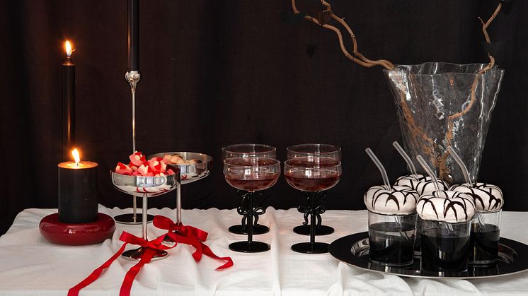 Elegant Halloween-dukning med svarta ljus, silverbägare med godis, röda drycker i glas med svarta rosetter. 