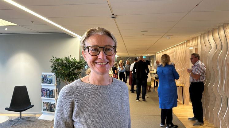 Lydia Kwak har en stickad grå tröja på sig, brunbågade glasögon, blont uppsatt hår och ler.