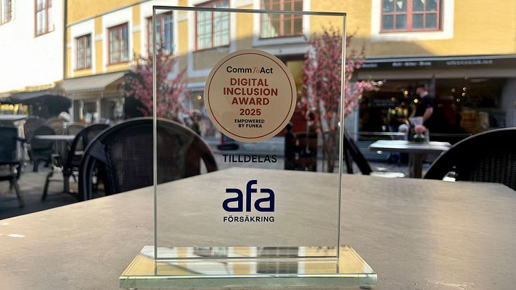 Priset i tävlingen CommToAct – Digital Inclusion Award 2025 står på ett ljusgrått bord med en äldre fasad i gult i bakgrunden