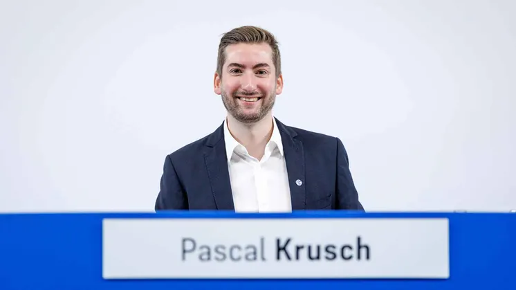 Pascal Krusch sitzt bei der Mitgliederversammlung hinter einem Namensschild