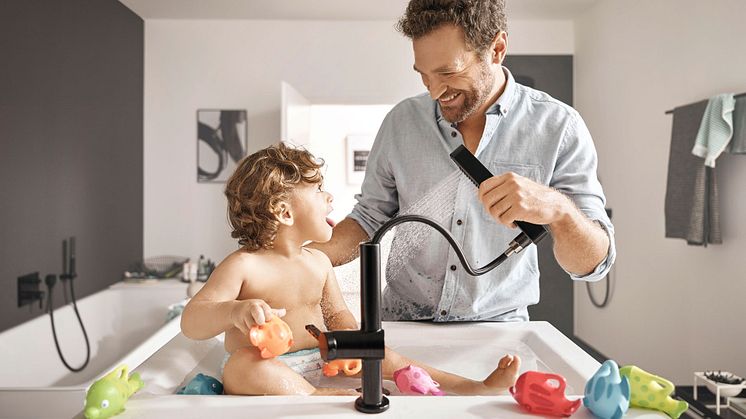 Ein Kind wird in einem modernen Waschtisch gebadet. Die neue Armatur von hansgrohe hat einen Schlauch.