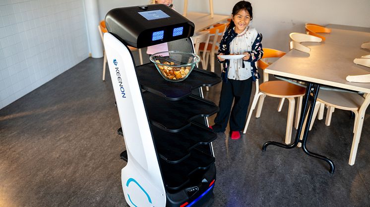 En måltidsrobot och en skrattande flicka i en skolrestaurang.