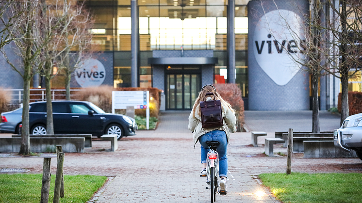 Vives-Hogeschool-Studierende radelt auf Campus mit Vives Logo.png