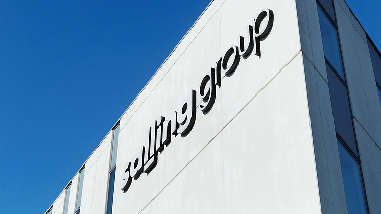 Ljusgrå fasad med Salling Group-logotyp mot klarblå himmel.