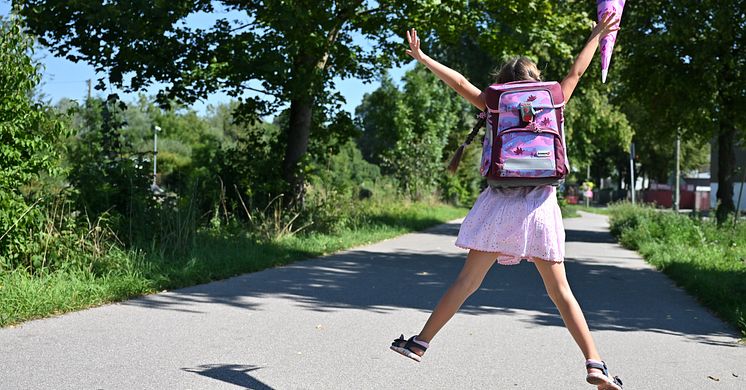 Mädchen mit Schulranzen und Schultüte freut sich und springt in die Luft.
