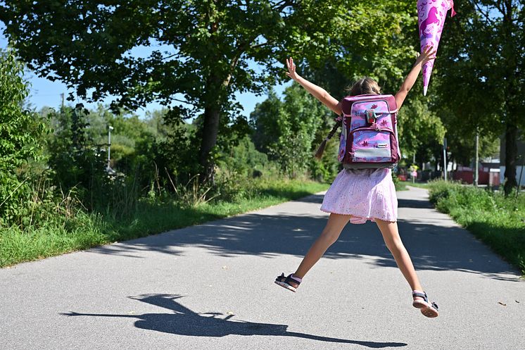 Mädchen mit Schulranzen und Schultüte freut sich und springt in die Luft.
