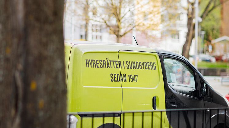 En av Förvaltarens skåpbilar med texten "Hyresrätter i Sundbyberg sedan 1947" står parkerad vid en gata intill ett träd.