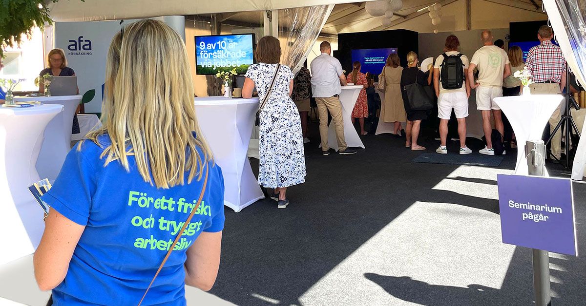 Seminarium pågår på Afa Försäkrings arena i Almedalen. I förgrunden syns en person med t-shirt med texten För ett friskt och tryggt arbetsliv och i bakgrunden pågår ett seminarium inne i ett stort tält med många i publiken.